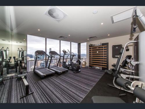 a gym with treadmills and ellipticals in a room with windows at LvL29 Rooftop Pool Carpark Netflix by Stylish Stays in Brisbane