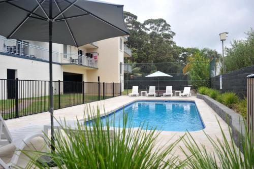 a swimming pool with an umbrella in a yard at Apollo Apartments Merimbula in Merimbula