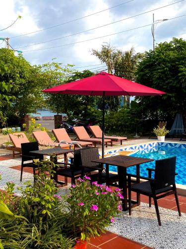 a red umbrella and tables and chairs next to a pool at Woodstock Beach Camp in Cat Ba