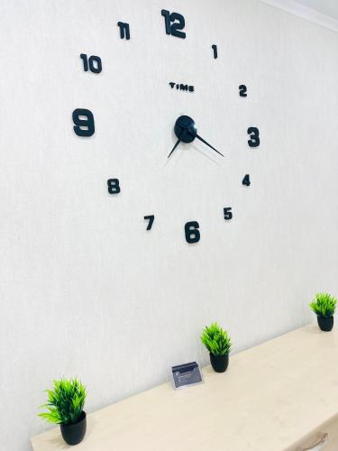 een klok op een witte muur met twee potplanten bij City in Oral
