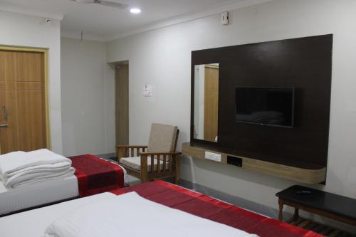 ein Zimmer mit zwei Betten und einem Großbildfernseher in der Unterkunft SRG Shivam Residency in Tiruvannāmalai