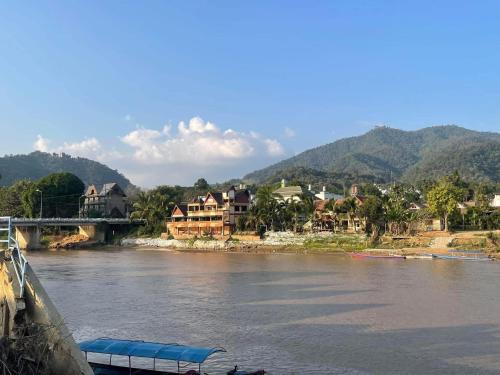 Un barco en un río con casas y un puente en ณิชาวิลล่า ริเวอร์ฟร้อนท์ บ้านท่าตอน Nicha Villa Riverfront BanThaton, en Mae Ai Chiang Mai