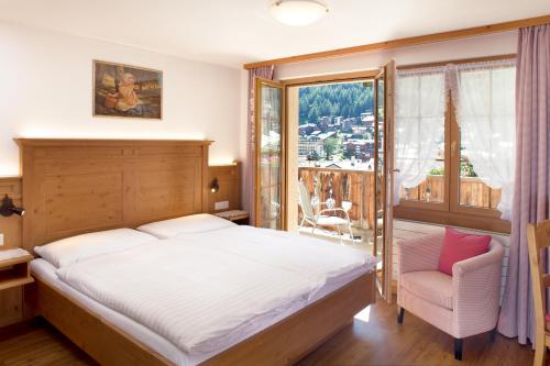 a bedroom with a bed and a chair and a window at Hotel Romantica in Zermatt