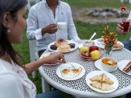 uma mulher sentada numa mesa com pratos de comida em Moustache Hostel Bir em Bir
