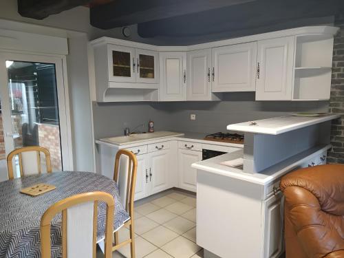cocina con armarios blancos, mesa y comedor en Gîte l'orée de la forêt légendaire, en Néant-sur-Yvel