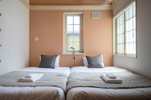 twee bedden in een kamer met twee ramen bij Guest House NANMO in Minami-jūichijō