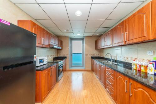 a kitchen with wooden cabinets and a black refrigerator at Spacious 3BR Seaview Duplex Perfect for Families in Ajman