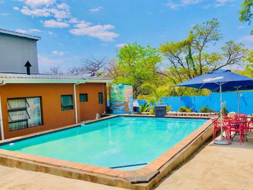 a swimming pool with tables and chairs and an umbrella at Woodpecker's Guest House in Hazyview