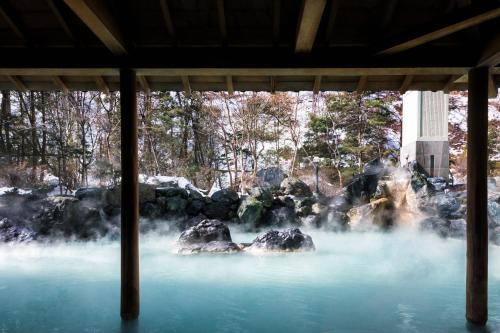 a pool of blue water with rocks and trees at Hotel Mahoroba in Noboribetsu