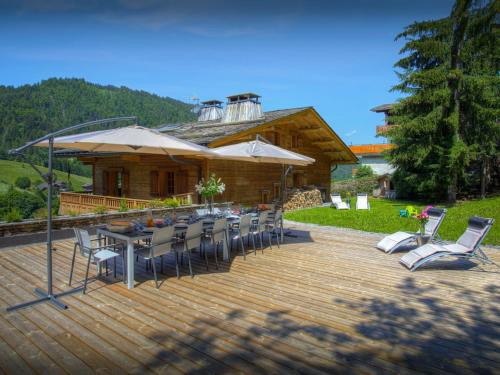 a wooden deck with chairs and a table and umbrella at Chalet Le Mousqueton - OVO Network in La Clusaz