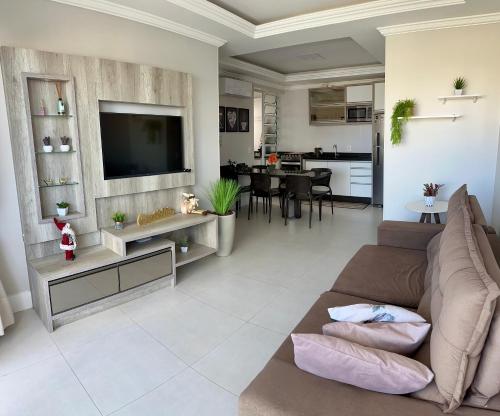 ein Wohnzimmer mit einem Sofa und einem Fernseher an der Wand in der Unterkunft Apartamento na praia de Palmas à 200m do mar in Governador Celso Ramos