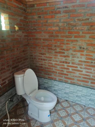 a bathroom with a white toilet in a brick wall at Pengaringan Cottage Cotol in Gitgit