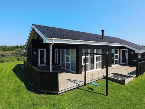 a black house with a wooden deck in the grass at 6 person holiday home in Hirtshals-By Traum in Hirtshals