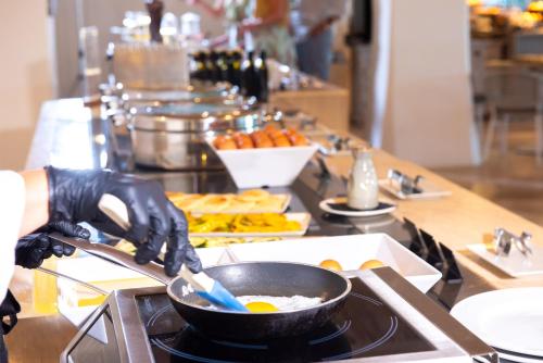 Una persona con guantes negros cocinando comida en una sartén sobre una estufa. en AMASEA Resort, en San Teodoro