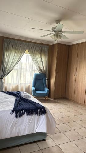 a bedroom with a bed and a blue chair and a ceiling fan at The N1 Farm Place in Pretoria