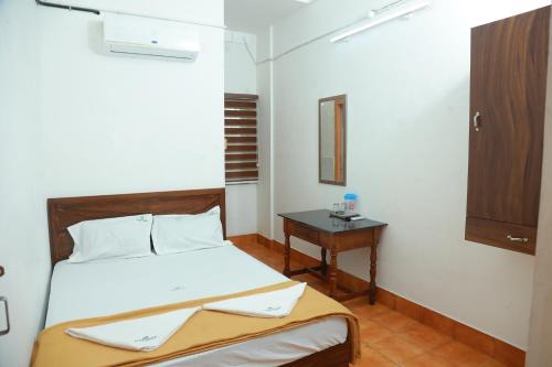 une petite chambre avec un lit et une table dans l'établissement Vinayaka Tourist Home, à Kozhikode