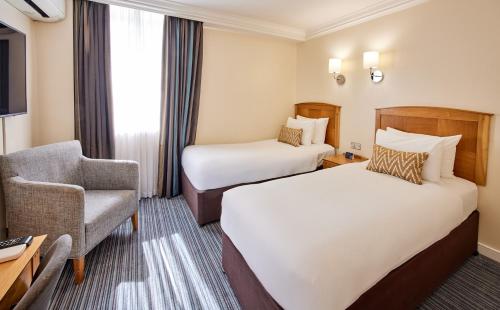 a hotel room with two beds and a chair at Thistle London Heathrow Terminal 5 in Hillingdon