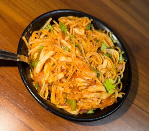 a black bowl of food with noodles and broccoli at Hotel Narayan Vilas , Jaipur in Jaipur