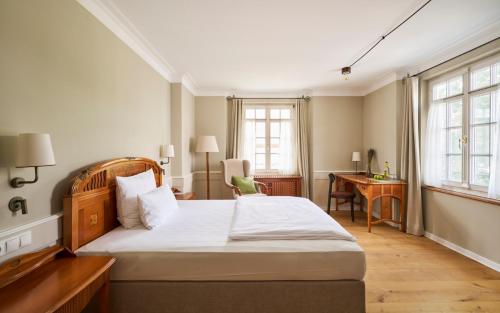 a bedroom with a bed and a desk and windows at Hotel Gutsgasthof Stangl in Neufarn
