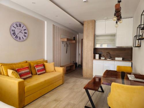 ein Wohnzimmer mit einem gelben Sofa und einer Uhr an der Wand in der Unterkunft Peak Montana Kopaonik in Kopaonik