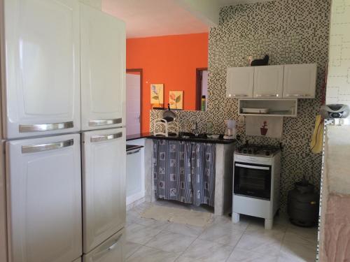 eine Küche mit weißen Geräten und einer orangefarbenen Wand in der Unterkunft Cruzeiro in São Pedro da Aldeia