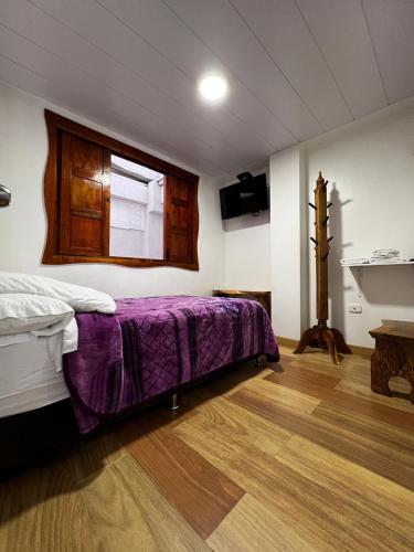 a bedroom with a bed with purple sheets and a window at Elizabetha Hostal in Salento