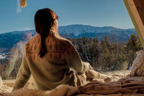 Eine Frau, die auf einem Bett sitzt und aus dem Fenster schaut. in der Unterkunft Alemiło mini - domek z balią i widokiem na Babią Górę in Zawoja
