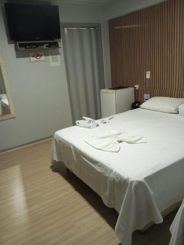 ein Schlafzimmer mit einem Bett mit weißer Bettwäsche und einem Flachbildfernseher in der Unterkunft Rocha's Hotel in Guarapuava