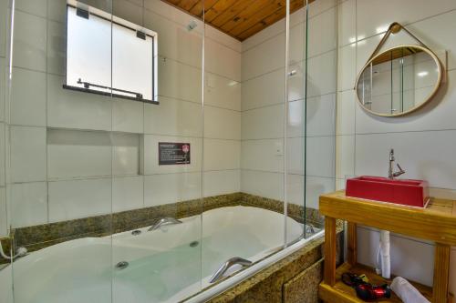 a bathroom with a tub and a glass shower at Pousada Chalé Suiço Bombinhas in Bombinhas