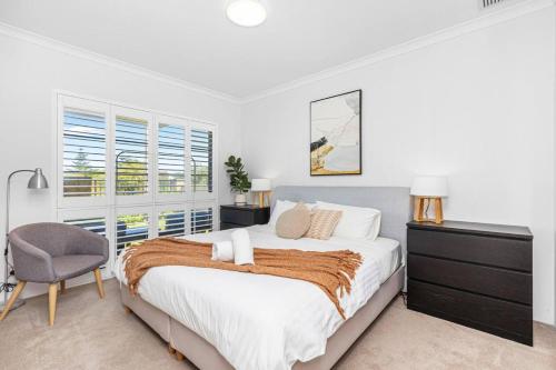 a white bedroom with a large bed and a chair at Coastal Retreat in Burns Beach in Kinross