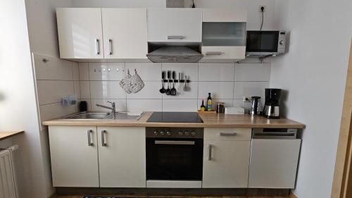 Una pequeña cocina con gabinetes blancos y un fregadero. en Gemütliche zwei Zimmer Wohnung am Rhein, en Weißenthurm