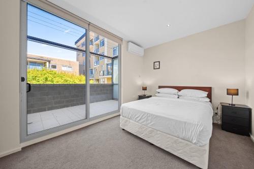 キャンベラにあるSpacious Apartment with Gym & Pool Accessのベッドと大きな窓のある寝室