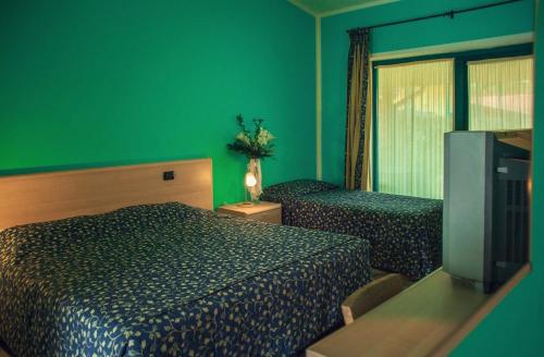 a green room with two beds and a television at Hotel Ristorante La Perla in Varallo Pombia