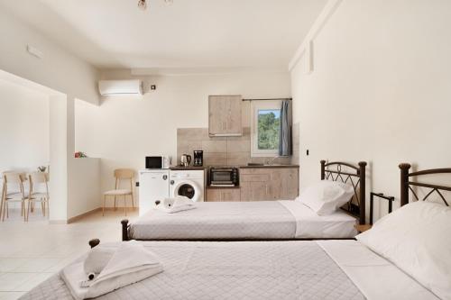two beds in a white room with a kitchen at Panagis Apartments in Argostoli