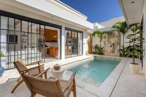 a swimming pool in a house with two chairs and a table at Villa Nida Premium by Tofino Villas in Uluwatu