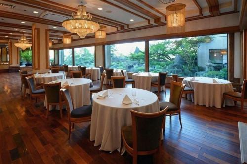 un restaurant avec des tables et des chaises blanches et de grandes fenêtres dans l'établissement Hotel Grand Shinonome, à Tsukuba