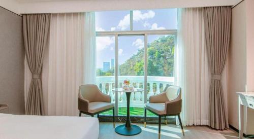 a bedroom with a bed and chairs and a large window at Zhuhai Dehan Hotel in Zhuhai