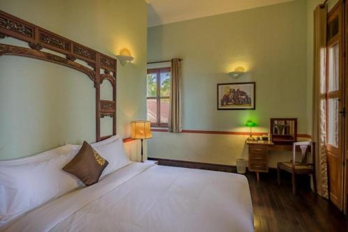 a bedroom with a white bed and a desk at Le Relais de Chhlong in Chhlong