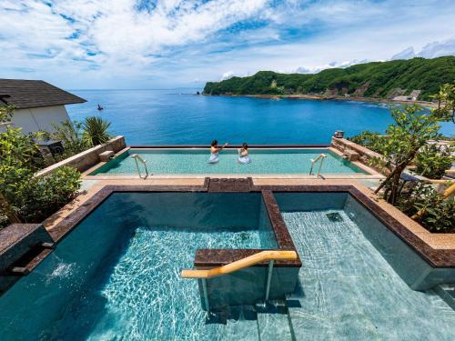 two people standing in a swimming pool overlooking the ocean at Mikazuki Sea-Park Hotel Awa Kamogawa in Kamogawa