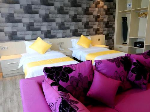 Una habitación con dos camas y un sofá con almohadas moradas. en Kidurong Inn, en Bintulu