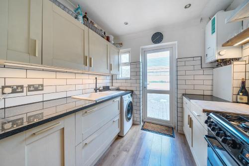 a kitchen with white cabinets and a washer and dryer at Entire Modern Apartment with Garden Near Underground Station in London