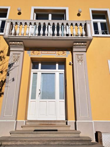 a yellow building with a white door and a balcony at Villa Emilia nelle Dolomiti in Domegge di Cadore