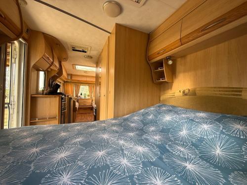 Un dormitorio en una casa rodante con una manta azul. en Caravanne 4 Pers Vue Sur L'étang, en Champsac