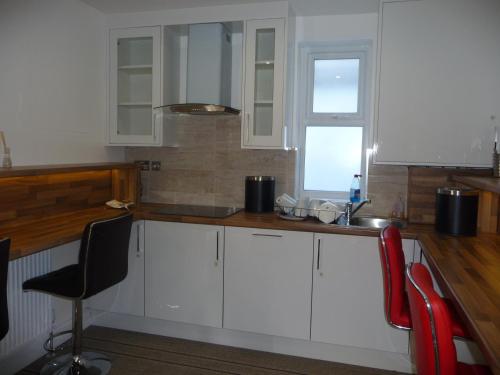 a kitchen with white cabinets and a red chair at Heathrow-Windsor Guest House in Slough