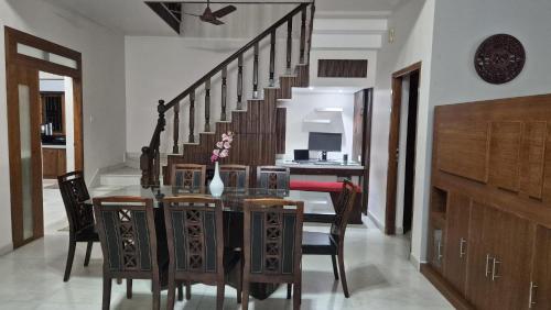 a dining room with a table and chairs and a staircase at Thistle Cosy Villa in Kozhikode
