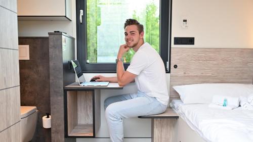 a man sitting at a desk with a laptop in a bedroom at Roatel Schkeuditz A9 my-roatel-com in Schkeuditz