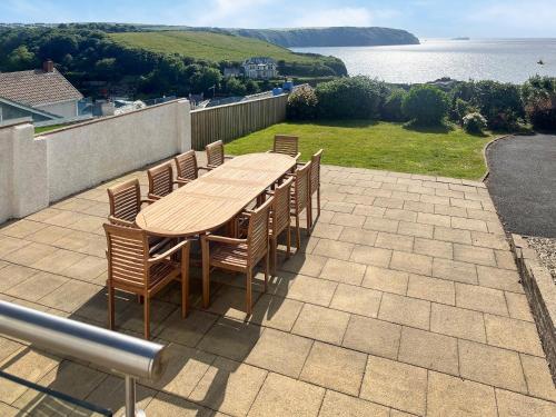 a wooden table and chairs on a patio overlooking the water at Upper White Gates in Little Haven
