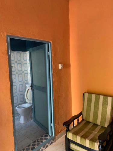 a bathroom with a toilet and a chair in it at Sumanguru Airport Studios in Busumbala