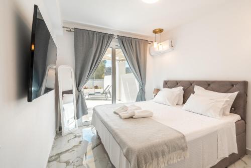 Cette chambre comprend un lit avec des draps blancs et une télévision. dans l'établissement Punta Mare Villa 4, à Karpathos
