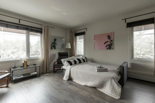 a bedroom with a bed and a chair and windows at Downtown - Rooftop patio - Free shuttle to ski Mountain in Mont-Tremblant